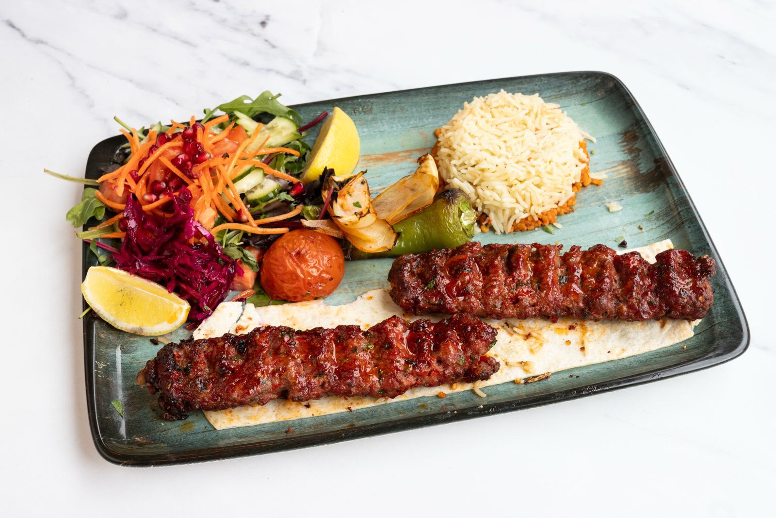 Two glazed adana kebabs fresh off the charcoal grill with rice, salad and grilled vegetables.