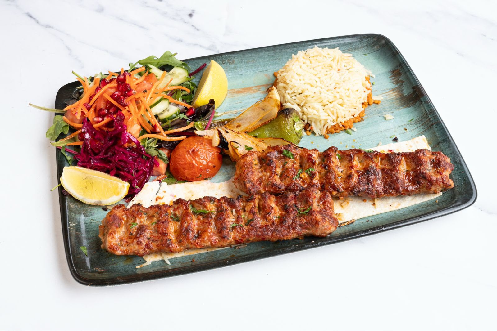 Hand-minced adana kofte kebabs grilled over charcoal, served with rice, salad and roasted vegetables.