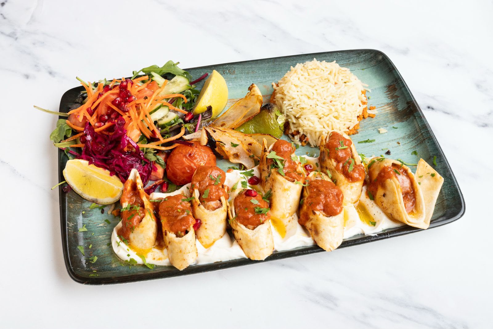 Beyti kebab wraps sliced over yogurt with tomato sauce, served with rice and salad.