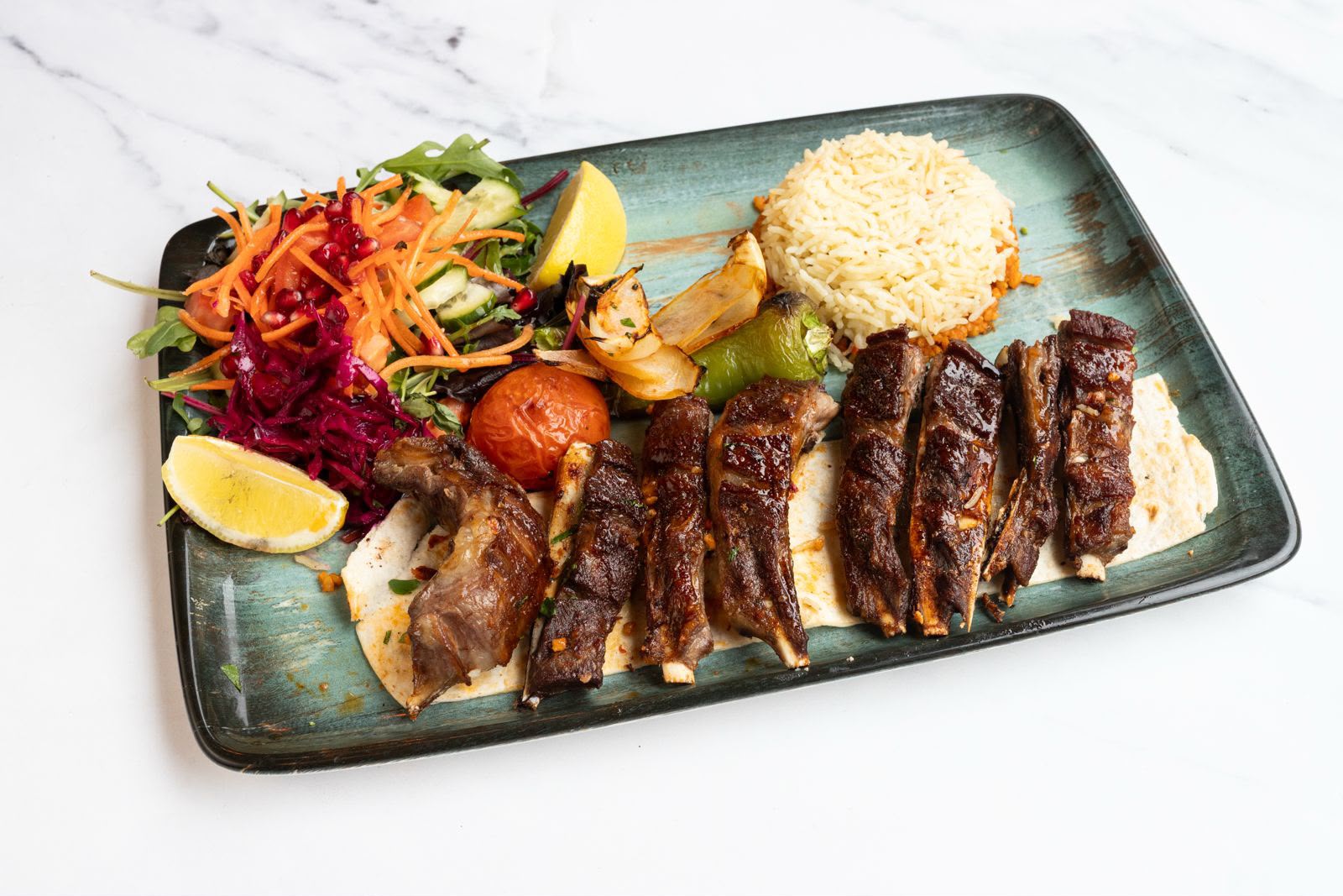 Sticky char-grilled lamb ribs on flatbread with rice, salad and roasted vegetables.