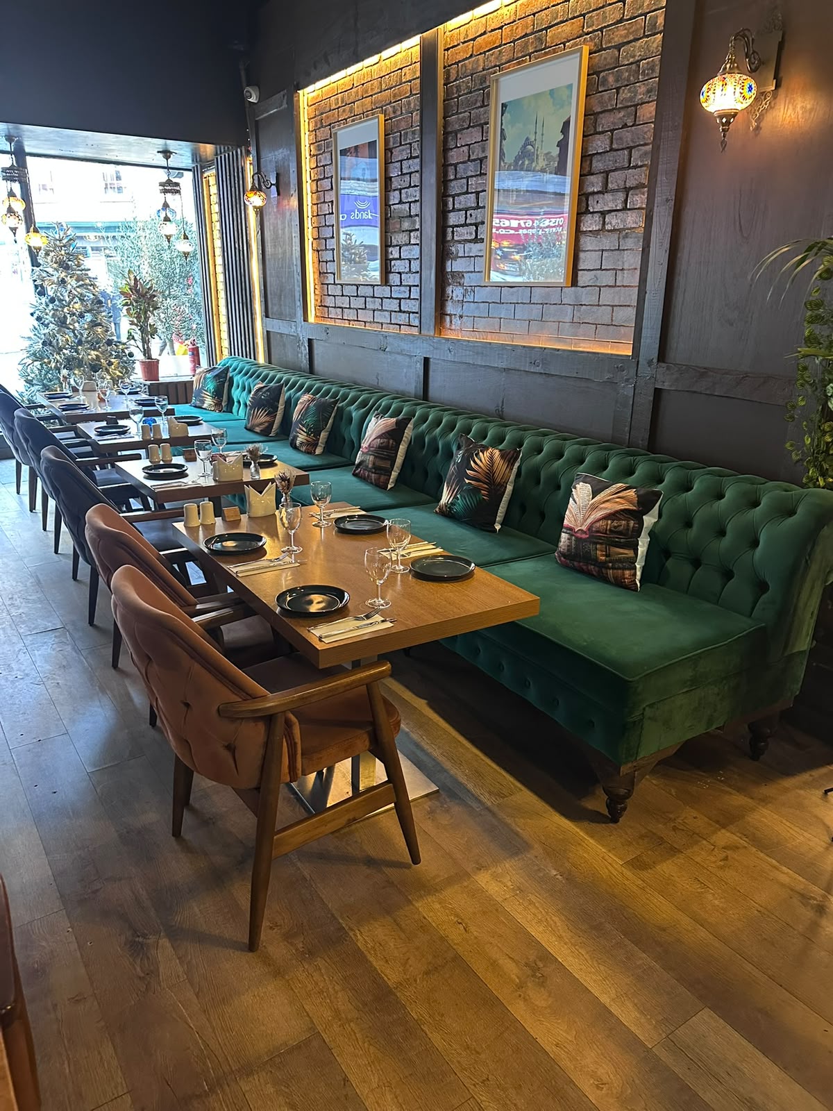 Green Chesterfield banquette and laid tables by the window in daylight at The Kervan.