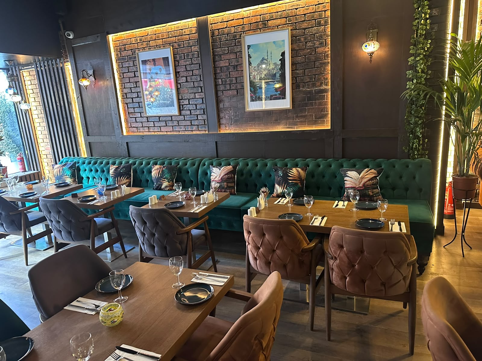 Emerald velvet banquette seating against exposed brick with framed art and mosaic lamps at The Kervan.