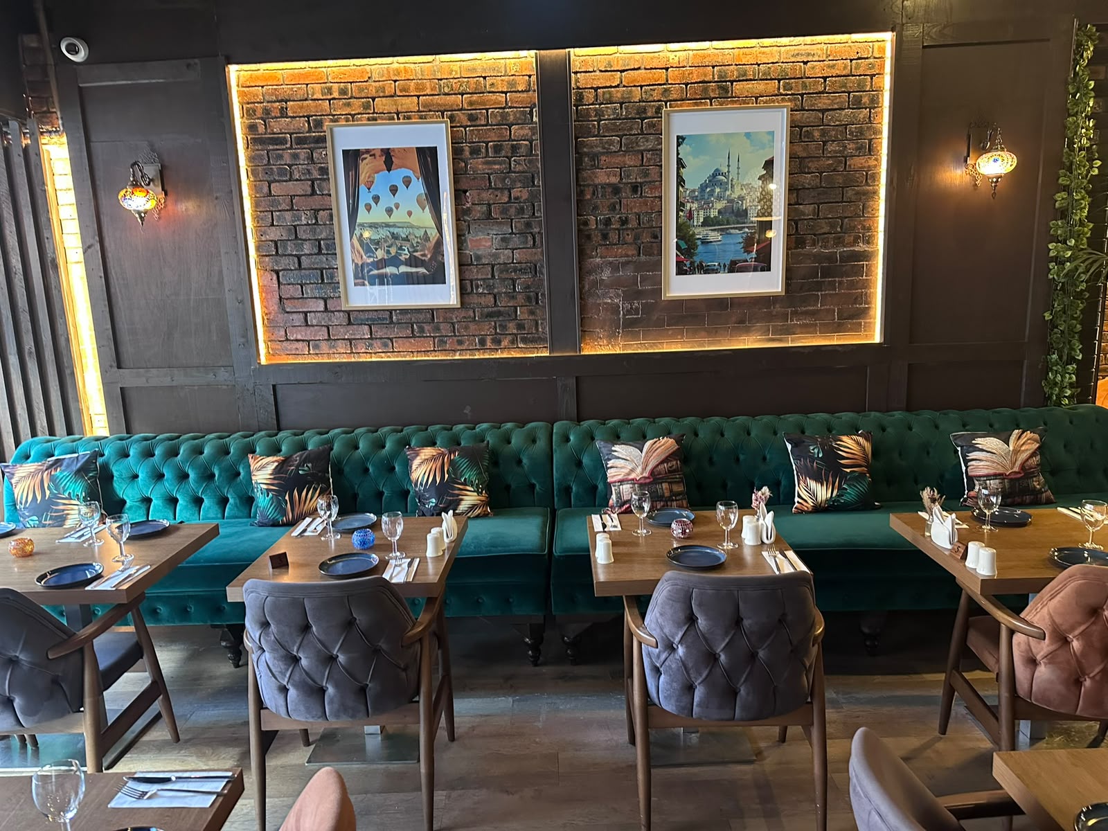 Laid tables and velvet seating beneath framed Istanbul and Cappadocia prints on backlit brick at The Kervan.